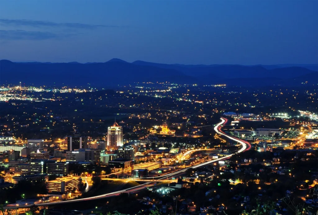 Illuminated city skyline and highway at night with mountains on the horizon